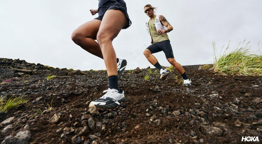 Two people running across loose terrain in Hoka trail runners